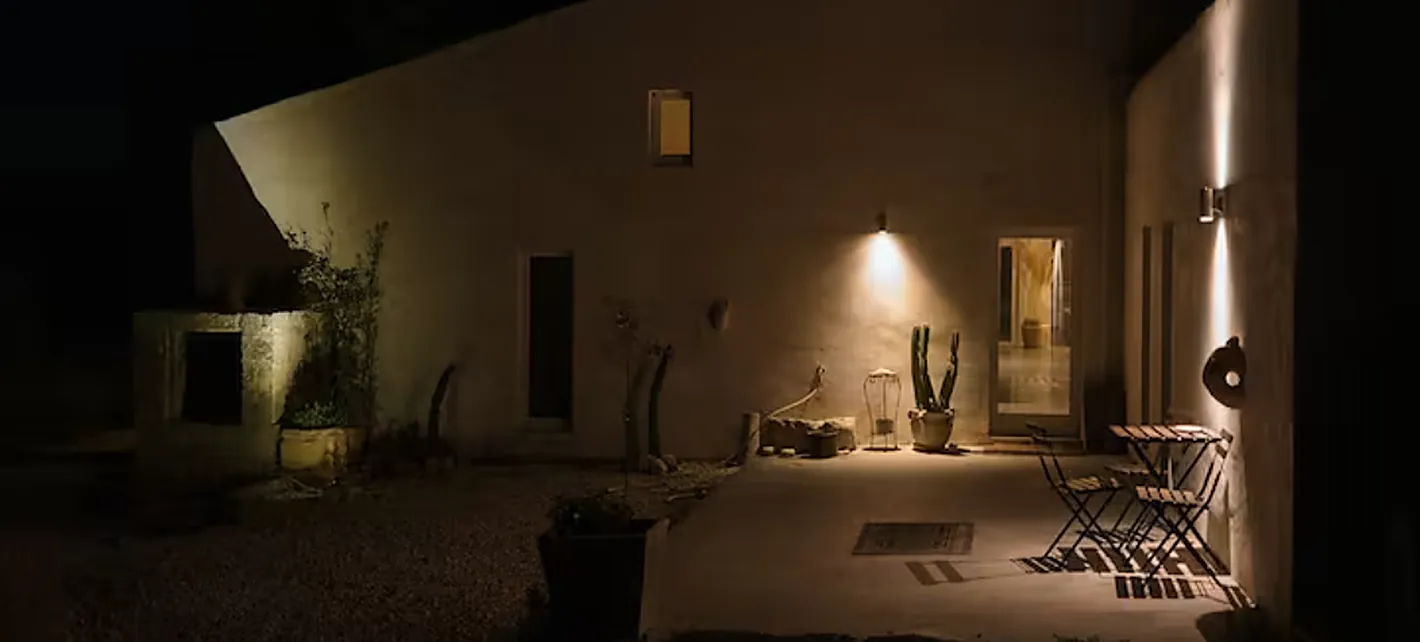 The farmhouse at night, its white walls washed by warm lamplight, chairs set out on the courtyard
