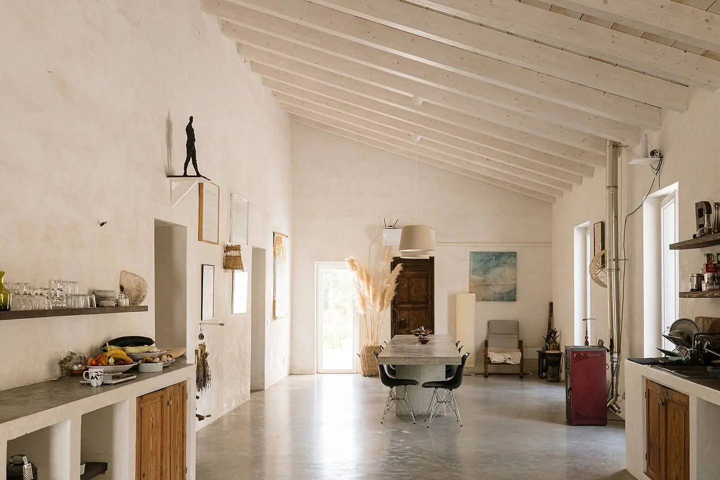 The long shared kitchen: white beamed ceiling, polished concrete floor, wooden cabinets and open shelves