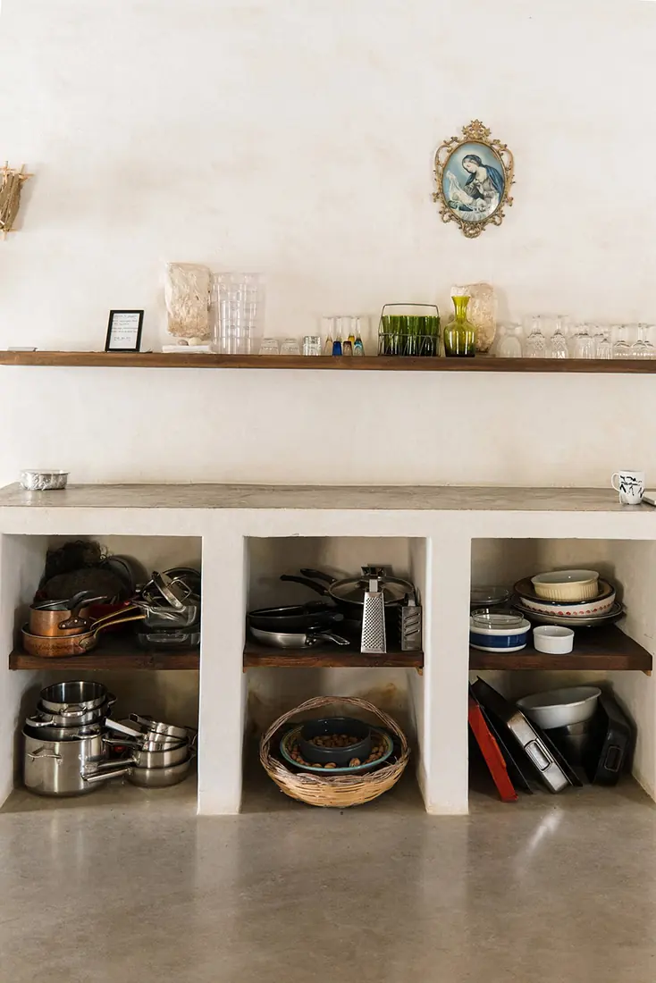 Open plaster shelves stacked with pans, bowls and rows of coloured glasses