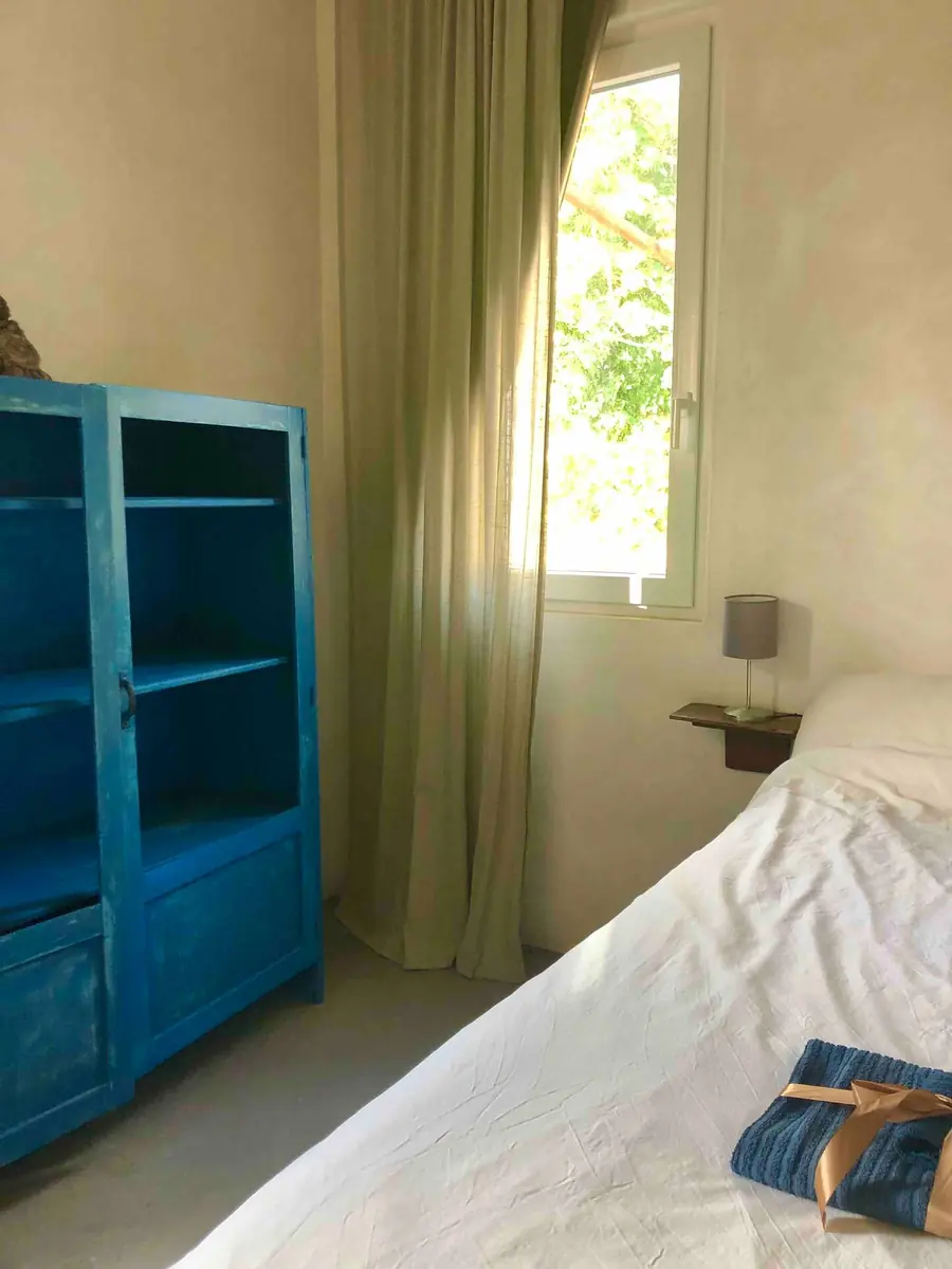 The tall blue-painted cabinet beside the bed in Room 2, with the green curtain at the window